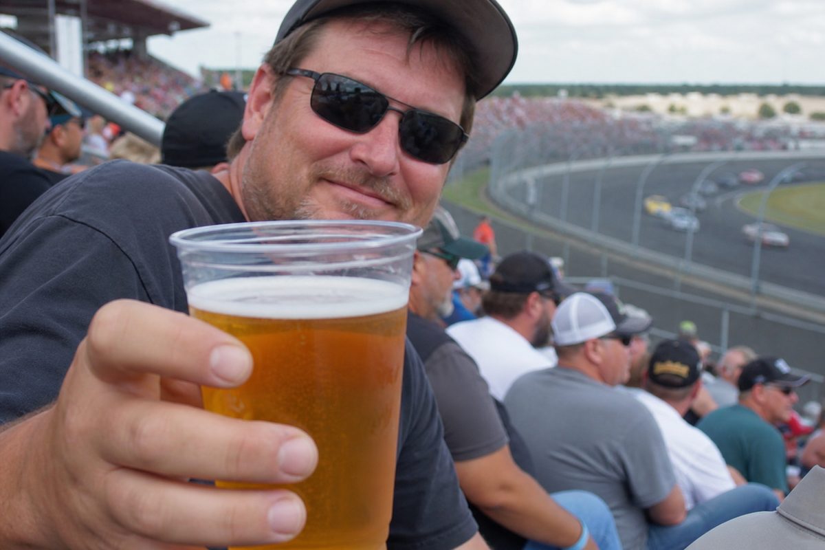 Adult race fan offering a plastic cup of amber ale