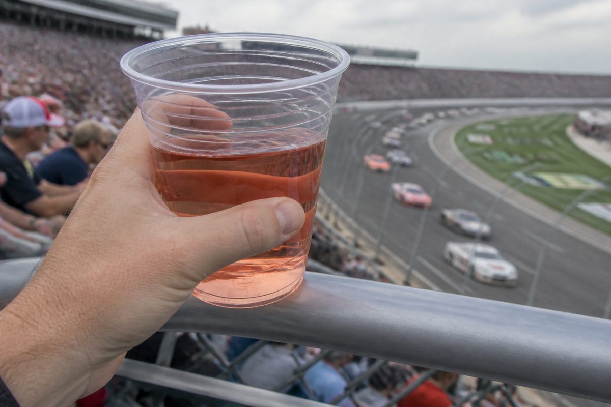 Plastic cup of rosé held over a racetrack railing