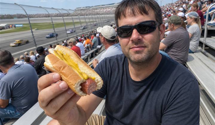 Race fan holding a partially eaten mustard hot dog in the grandstands