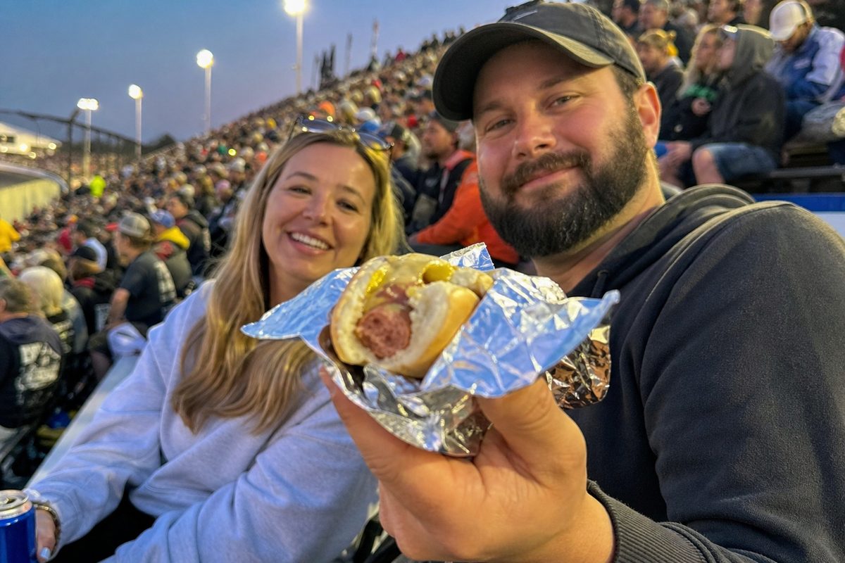 Two race fans offering a foil wrapped hot dog