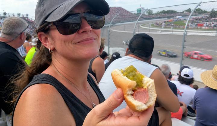 Race fan holding a partially eaten relish hot dog in the grandstands