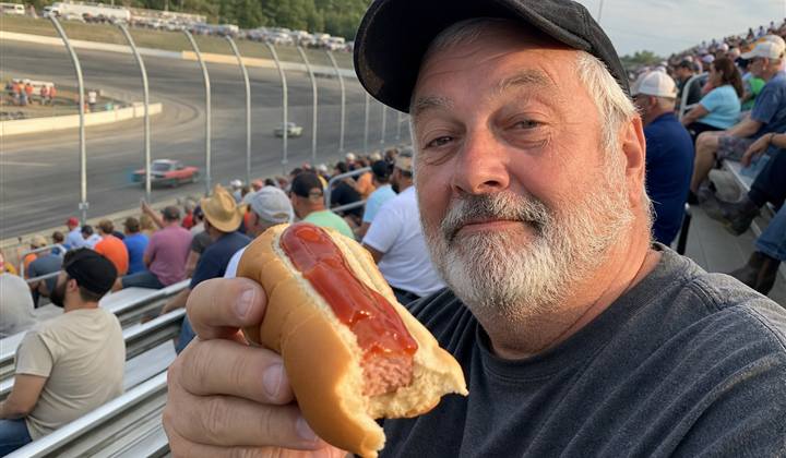 Race fan holding a partially eaten ketchup hot dog in the grandstands