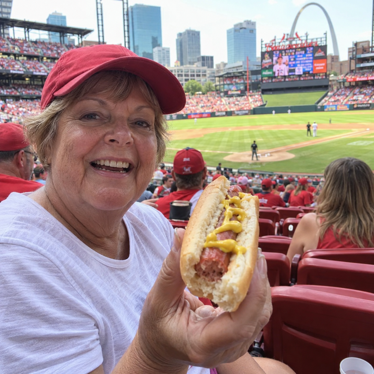 Older baseball fan in a red cap holding a half-eaten mustard hot dog