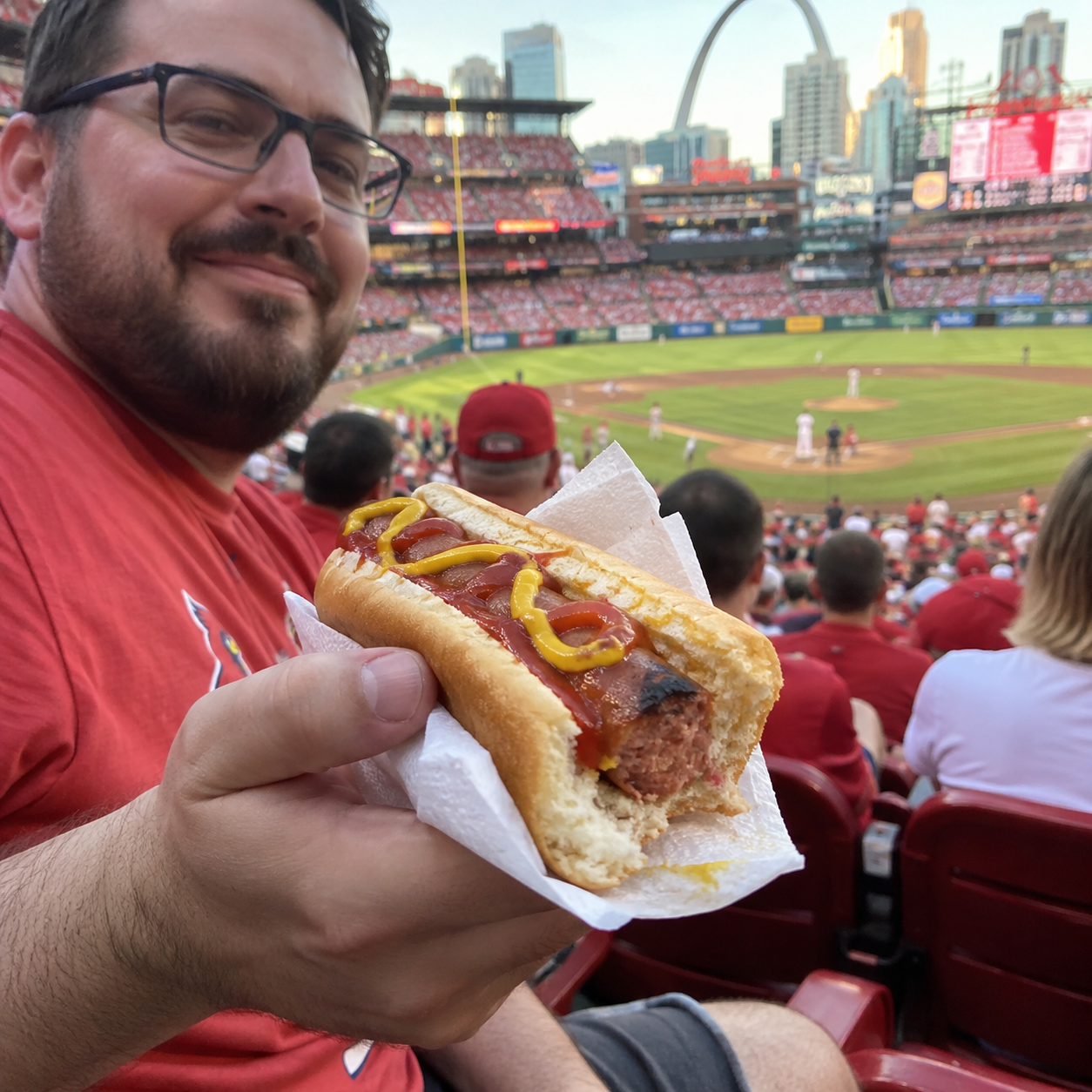 Fan with glasses holding a partially eaten hot dog at the ballpark