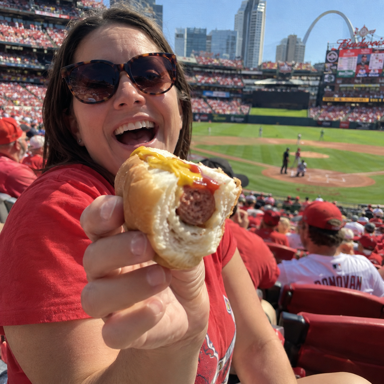 Woman in red holding a small remaining hot dog at a baseball game