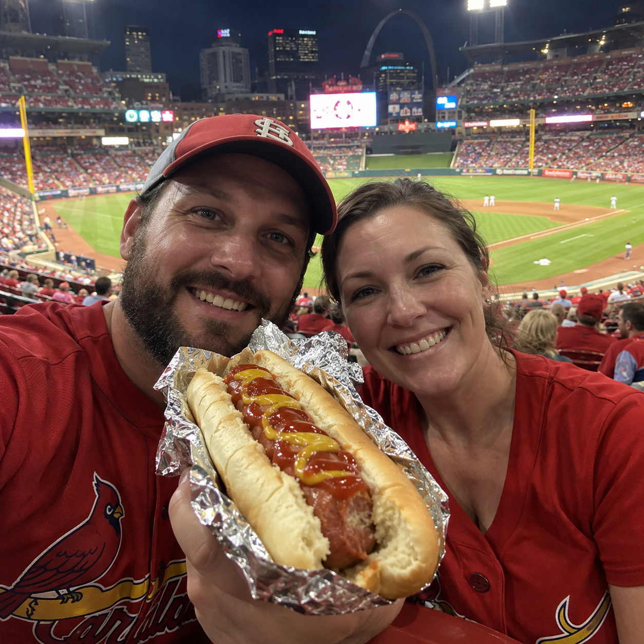 Two baseball fans holding a partially eaten foil-wrapped hot dog