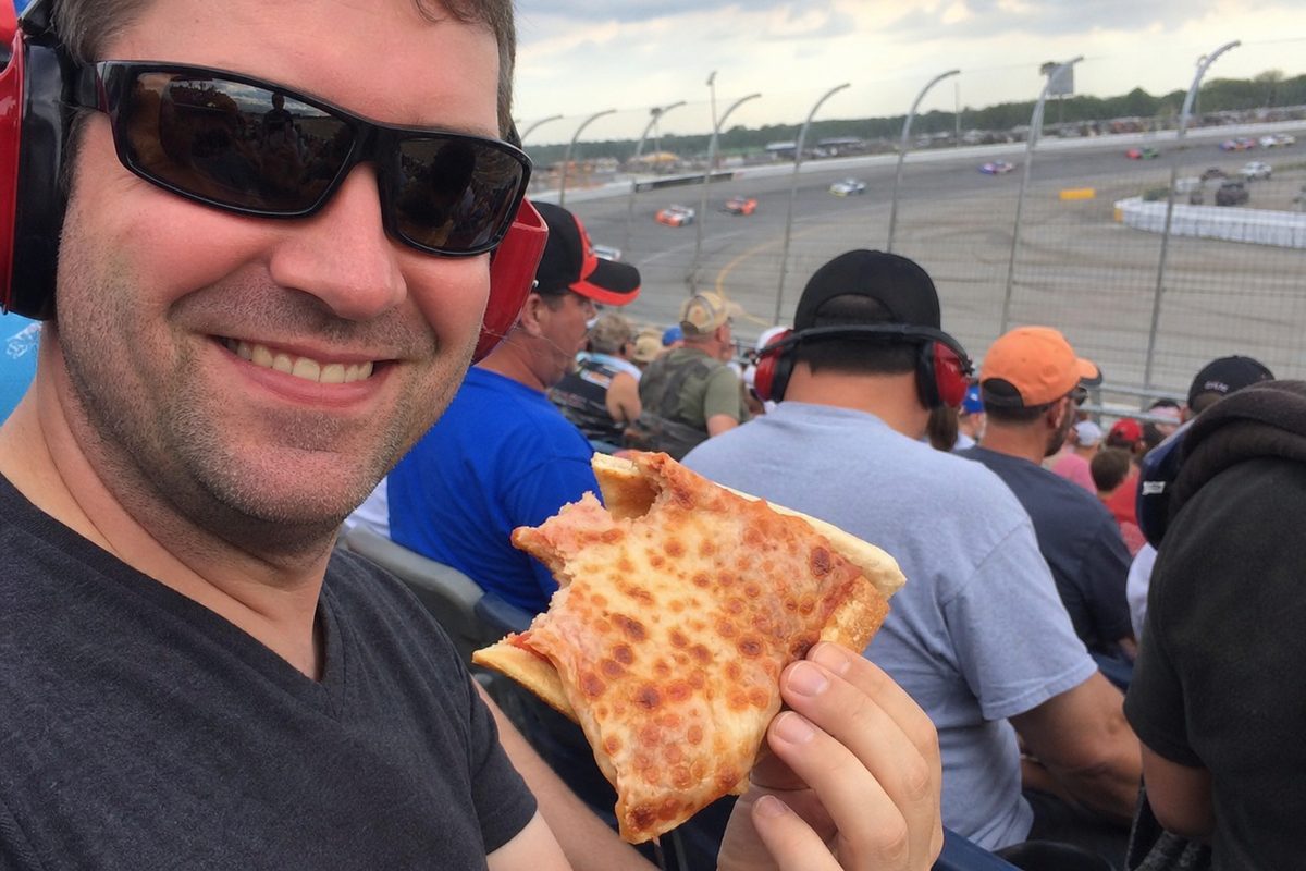 Race fan holding a folded partially eaten cheese pizza slice